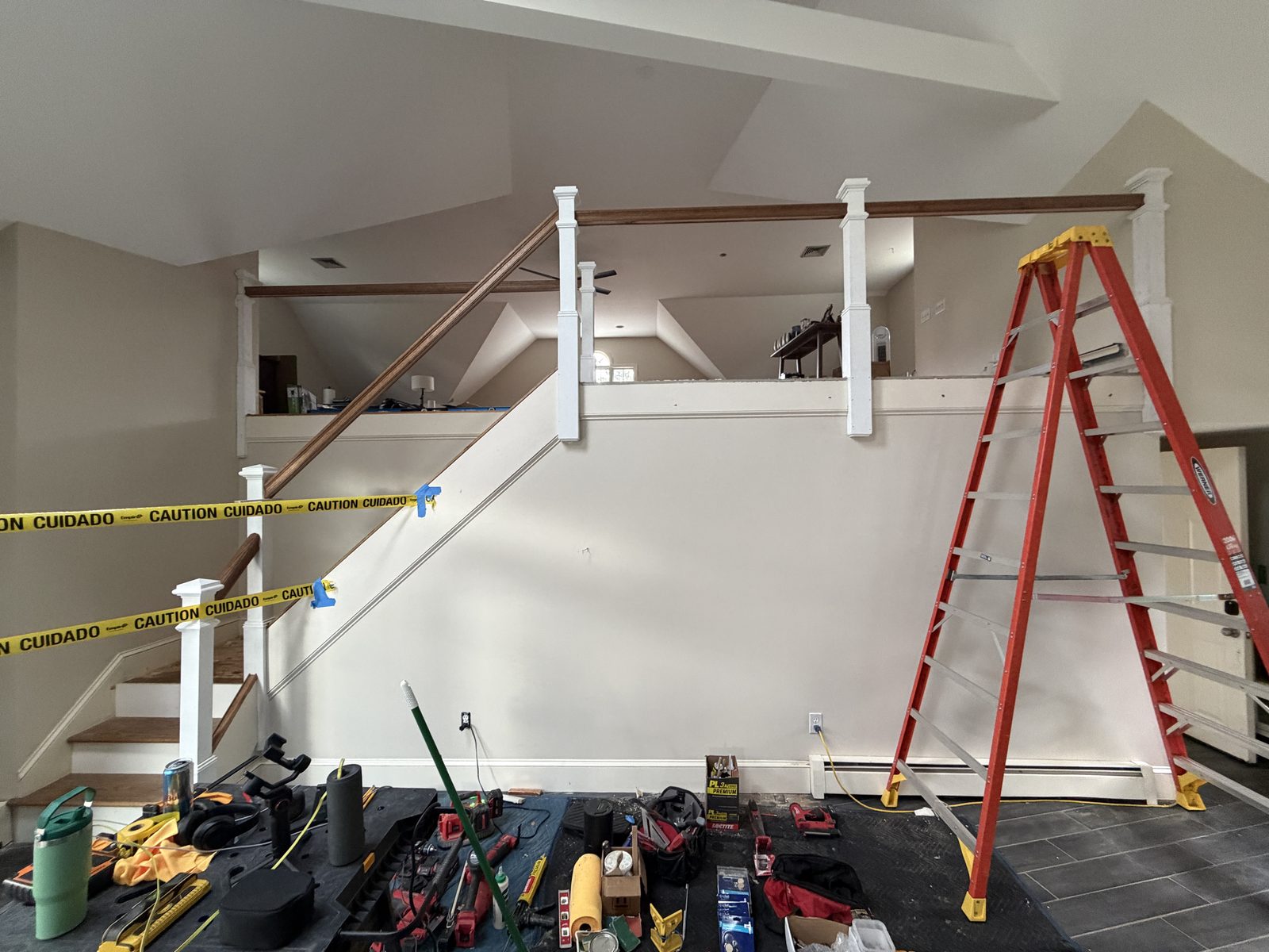 Newel posts and an angled handrail set on the Rehoboth staircase before the balusters were installed, with caution tape, protected floors and tools in place.